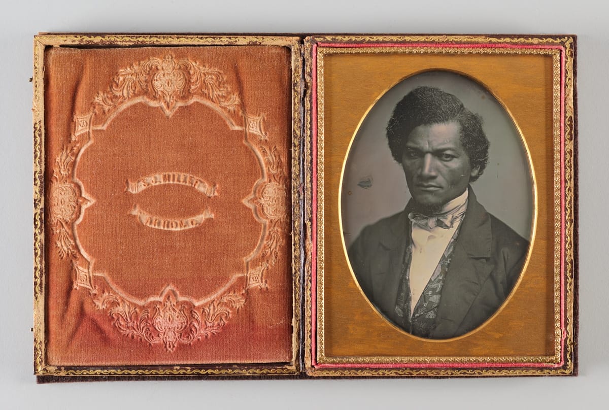 Historical black and white photographical portrait of Black man in a suit, gold frame.