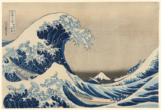 A towering blue-and-white wave with claw-like curls of foam arches over three long, narrow boats of crouching rowers, while snow-capped Mount Fuji sits small and low in the distance under a pale sky.