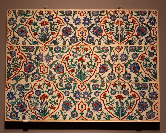 Panel of glazed tiles with a repeating pattern on a white ground: red-outlined medallions and curving leaves frame blue and red flowers, carnations and tulips on green stems.