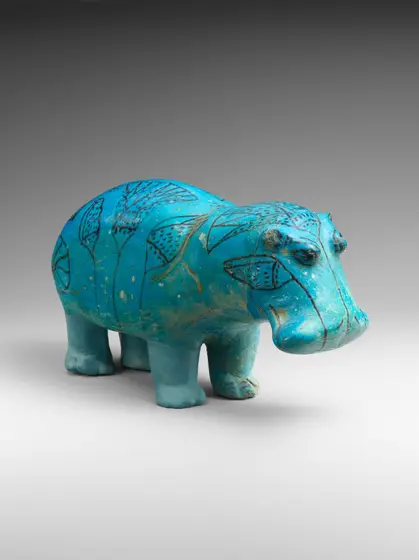 A small turquoise-blue faience hippopotamus standing on four stubby legs, its body painted in black with lotus flowers, buds and leaves, as if it were wading among river plants.